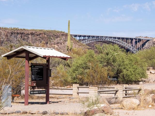 A kiosk at Burro Creek Campground with a desert environment and bridge in the background