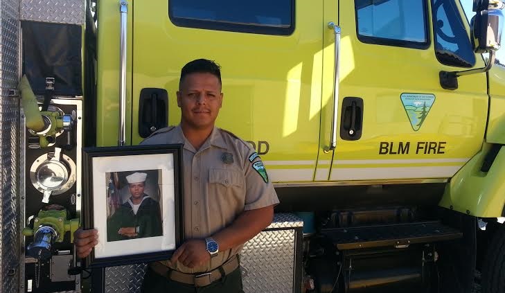 A BLM employee stands next to a firetruck, holding his military photo.  BLM photo.