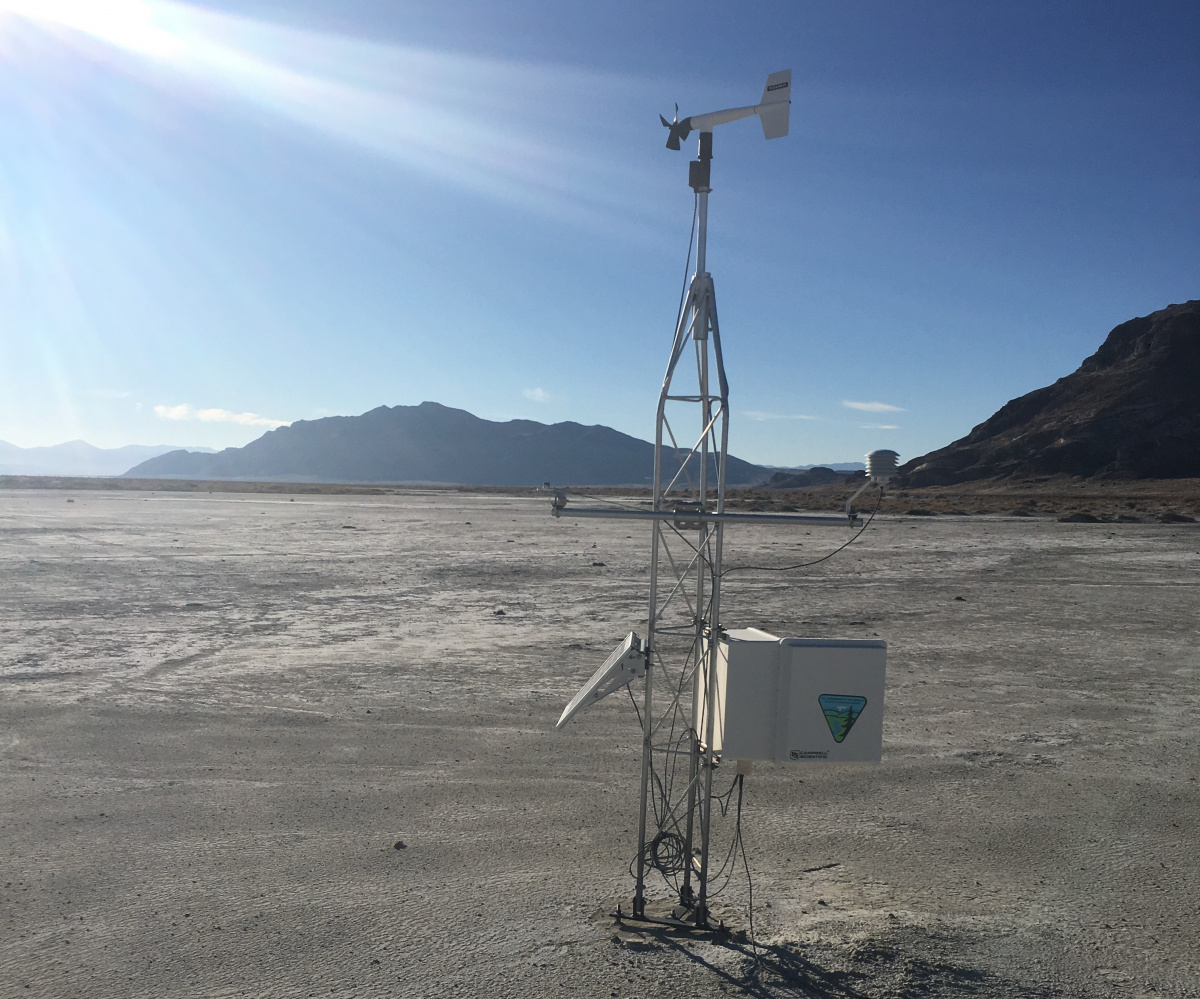 A weather station in a dry desert landscape with mountains looming and rays of sunshine beating down.
