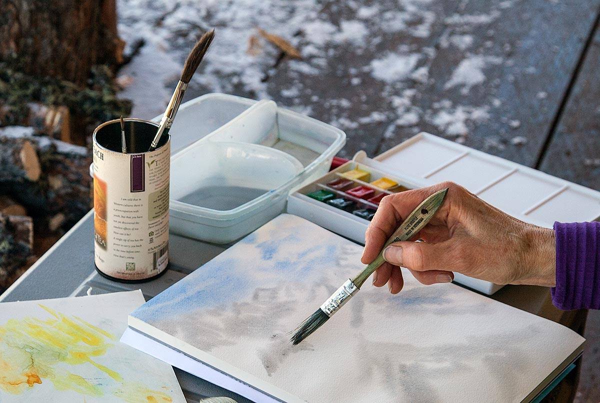 Close up photo of artists hand painting mountains with water colors at Windy Gap Cabin.