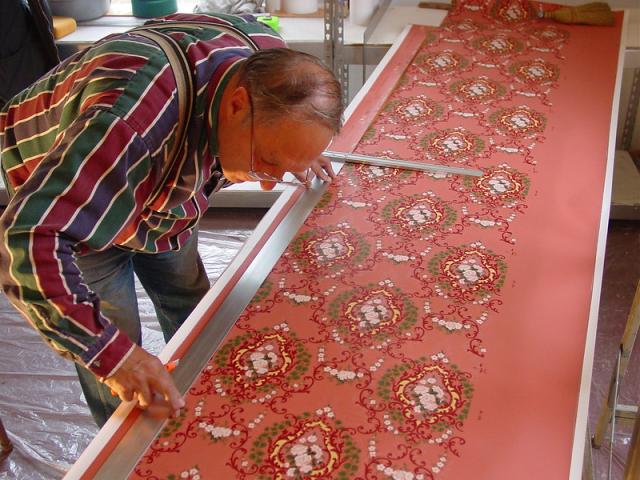 Man measuring ornate red wallpaper