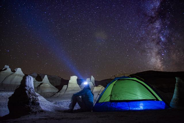 Hiker with headlamp looks up towards starry night over rock formations