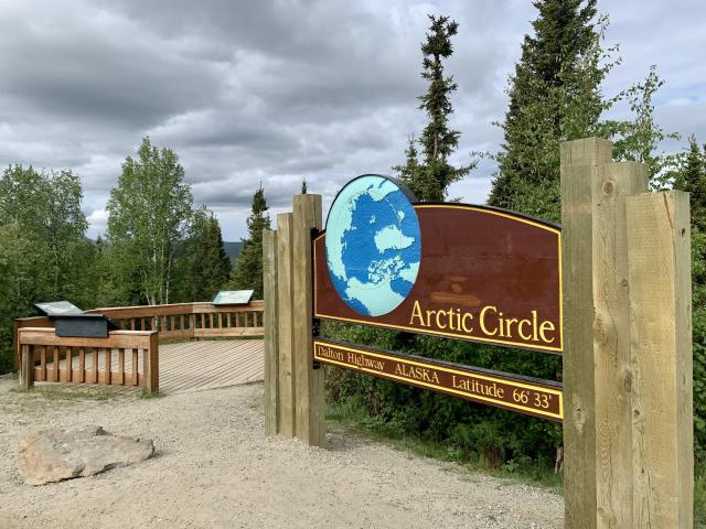 A wooden sign for the Arctic Circle, Dalton Highway, Alaska, Latitude 66° 33’. Depicts north pole of the earth with the arctic circle shown in a dashed line.