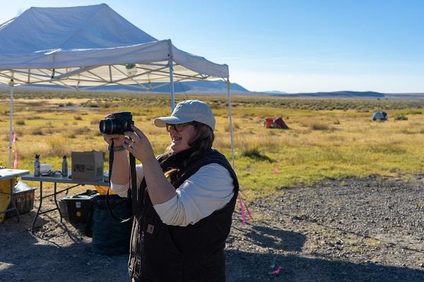 A woman holds a camera next to a tent. 