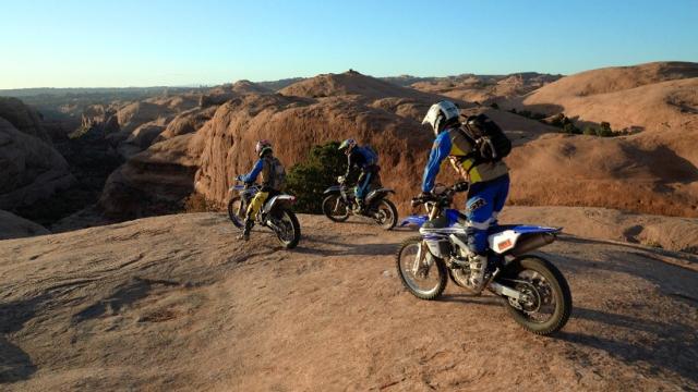 Three motorcyclists ride on slickrock overlooking sandstone fins in Sand Flats Recreation Area.