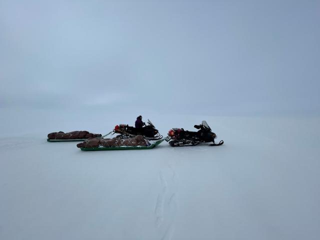 Snowmachines towing sleds with gear wrapped in tarps. 