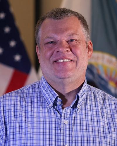 person with short hair wearing a collared shirt posing in front of the American flag