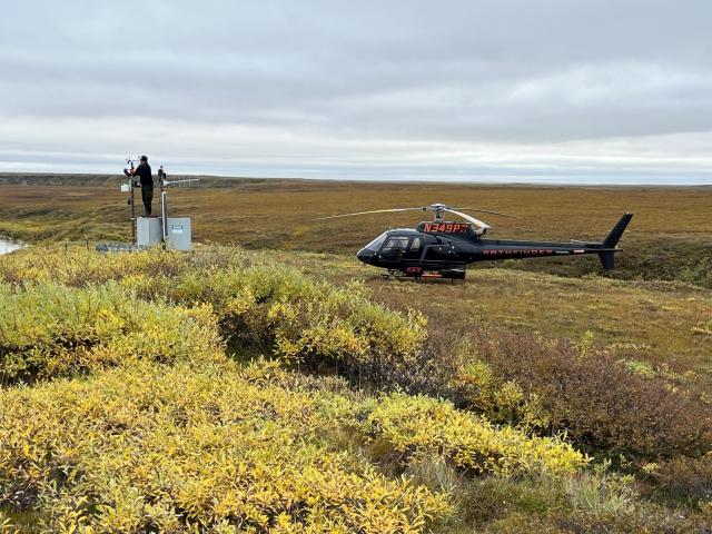 two hydrologists work near a helicopter to replace the wind sensor on the river gage.
