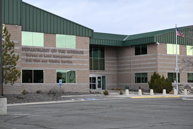 A brick building that is home to the Nevada State Office for the Bureau of Land Management located in Reno, Nevada sits behind the U.S. flag as the sun rises.