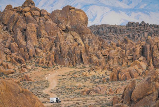 A silver camper at the base of rocky hills.