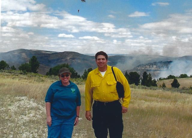 Photo shows Rugwell standing outside with a BLM employee with smoke from a prescribed fire in the background.