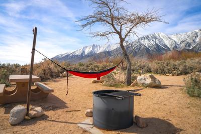 A camp site with a hammock and fire pit with mountains in the distance.