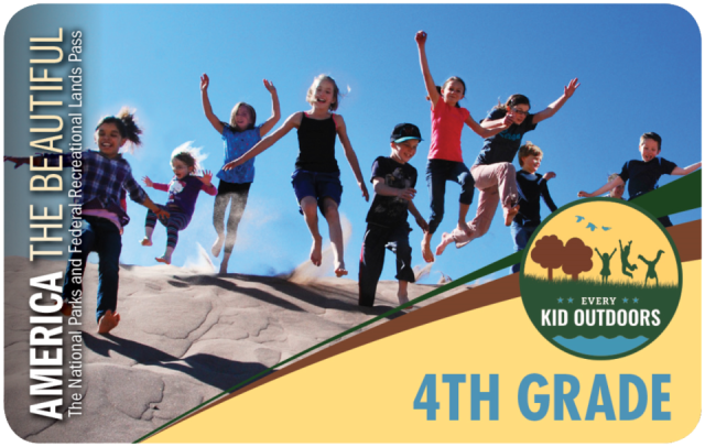 Photo of the Every Kid Outdoors Pass showing ten young children with bare feet jumping down a sand dune, most of them with their hands reaching up to the blue sky.