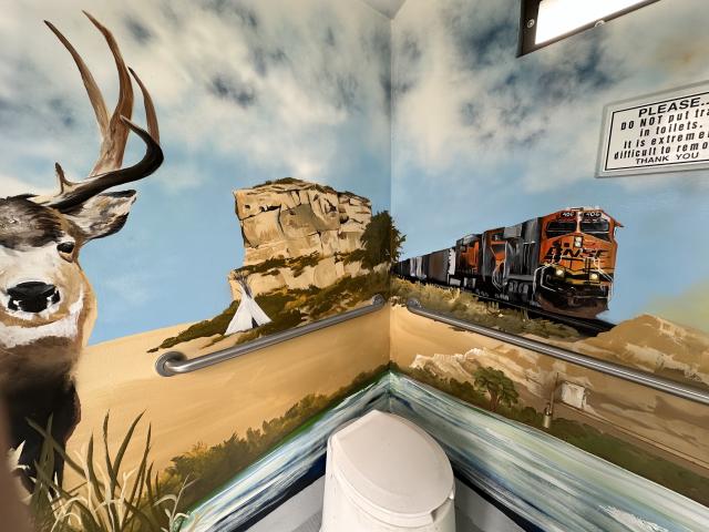 Full color mural on inside wall of vault toilet showing mule deer, teepee and train in front of Pompeys Pillar. 