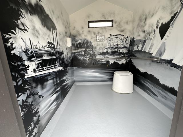 photo of a mural in blacks and grays on the inside walls of a vault toilet