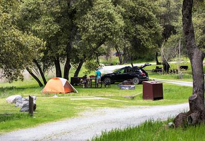 Campsite with orange tent, black sedan, picnic table and fire ring.