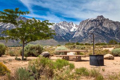A picnic table and fire pit with tall mountains in the background.