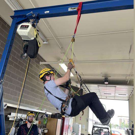 A person in a harness hangs by a rope from an overhead support.
