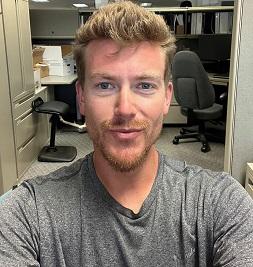 person in a gray shirt taking a selfie in an office setting