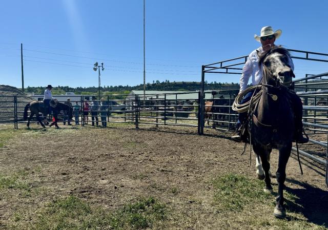 Photo: horse and rider walk toward photographer in a corral. 