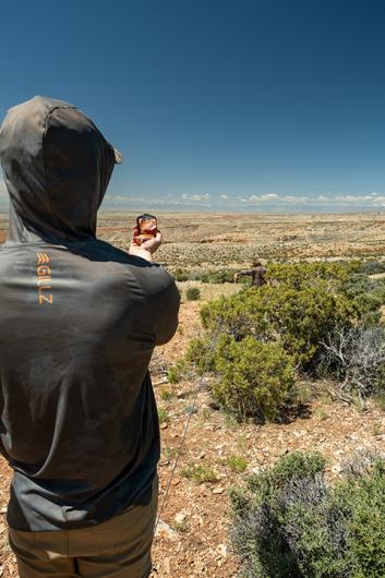 photo: looking over shoulder of person from the back who is wearing a hoodie and stretching arm over brush-covered hill