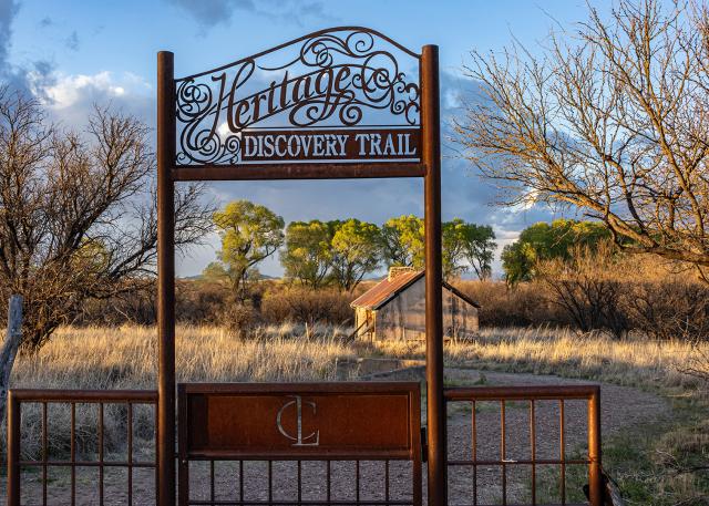 A gate to the Heritage Discovery Trail leads to a path along a grassy area of the Las Cienegas National Conservation Area.