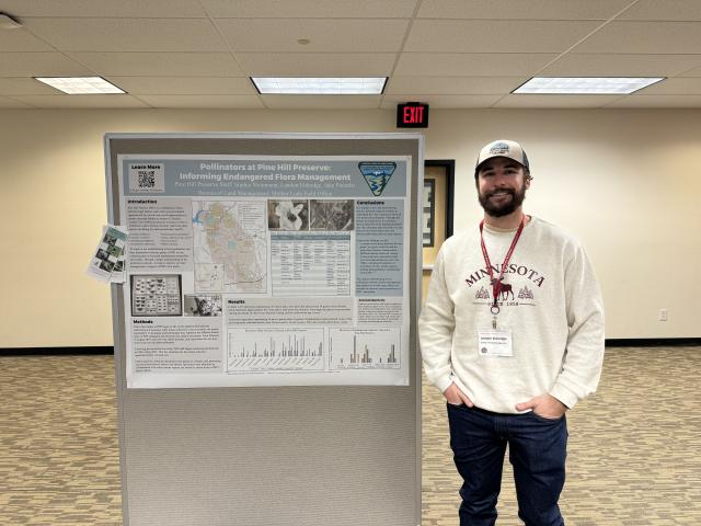 Landon Eldredge stands next to a poster about pollinators at Pine Hill Preserve.