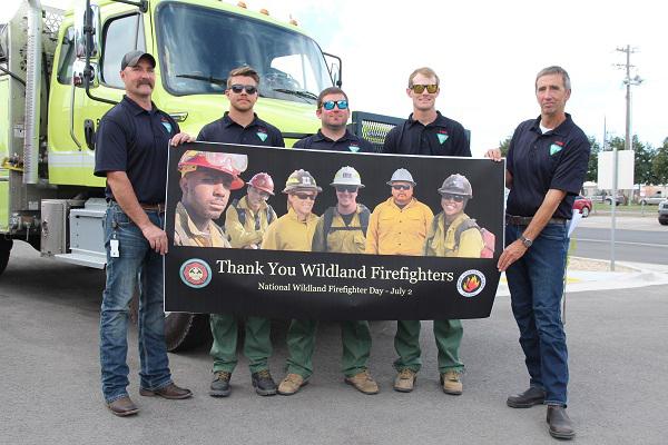 Five Caucasian men in blue polos with the BLM logo hold a sign saying "thank you wildland firefighters, national wildland firefighter day, July 2"