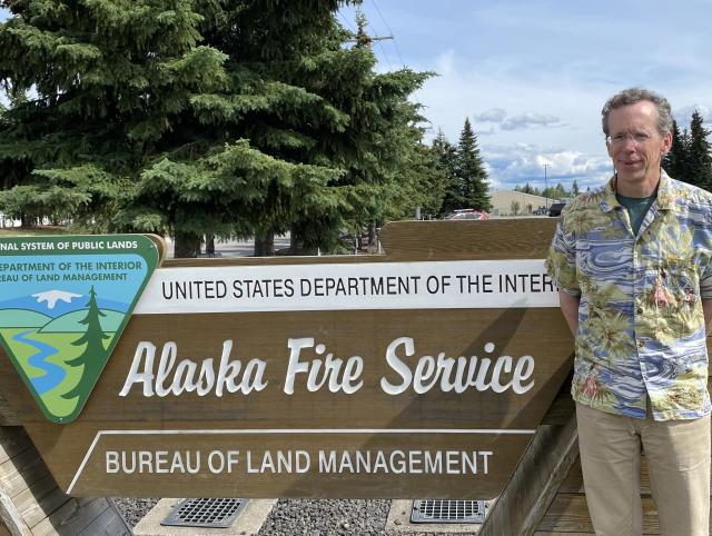 A Caucasian man stands next to a sign reading "Alaska Fire Service"