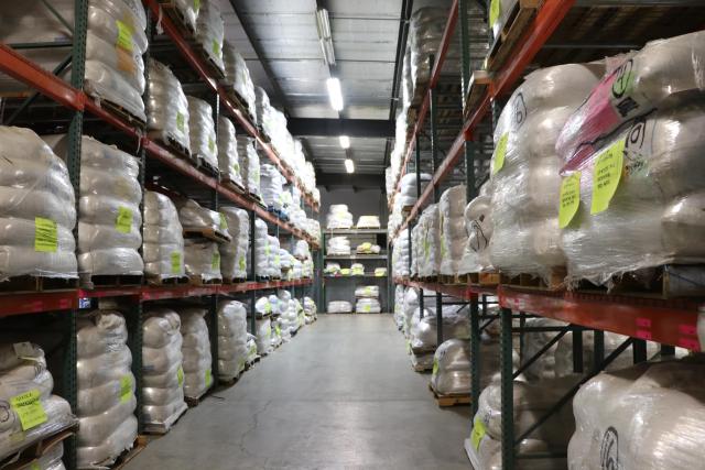 Warehouse shelves stacked to the ceiling with large packages wrapped in white plastic