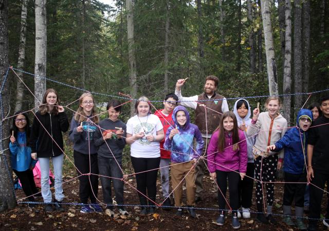 A group of people stand in front of a large rope spiderweb.