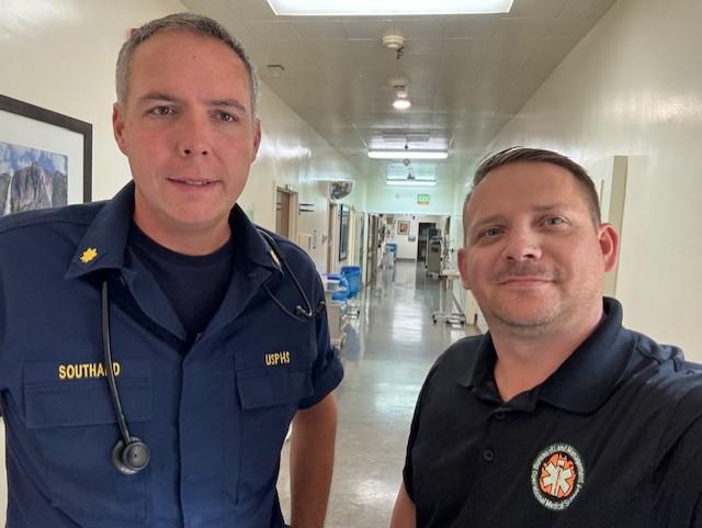 Two white men pose for a selfie in a hallway in a medical establishment