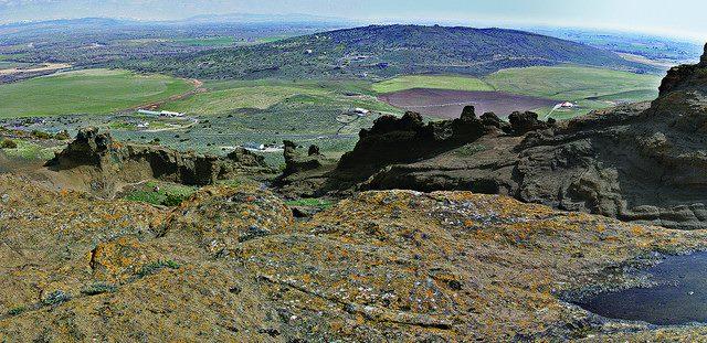 Landscape of North Menon Butte showing rocks, green fields and hills at the horizon.