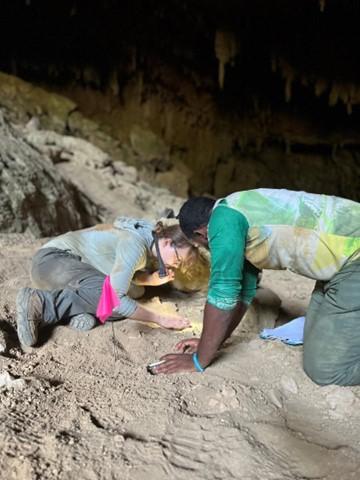 Two archaeologists documenting artifacts in a cave.