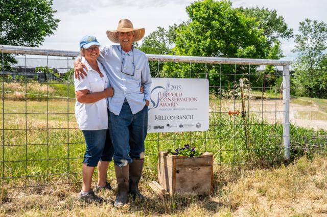 Two people Bill and Dana Milton standing in front of a gate at the Milton ranch