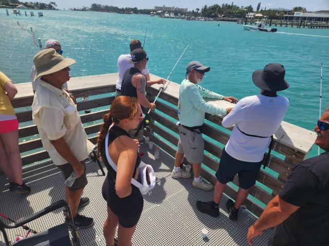 A group of men and women talking and fishing from a pier above the blue waters of Jupiter Florida