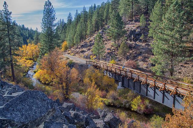 An old railroad bridge converted to a = bicycle trail along a creek in a forest with fall colors.