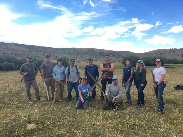 A group of people holding handsaws pose for a photo in a scenic area outdoors.