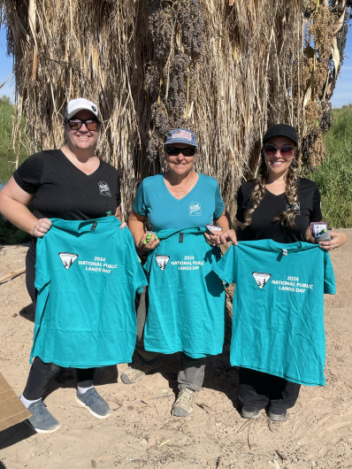 Three volunteers stand together displaying their t-shirts for cleanup efforts.