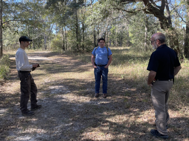 A teenager and two adults are seen standing and conversing. 