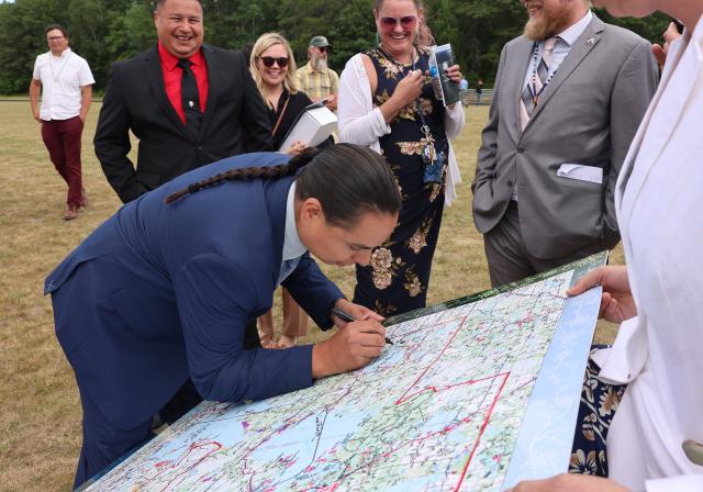 A man in a suit leans over a large map, signing it. 