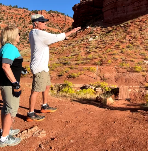 A couple stand in front of a bridge built over a wash in red rock country. 