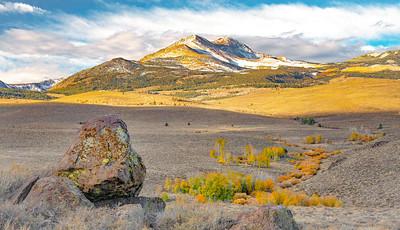 A line of yellow and orange aspens lead from a boulder in the foreground to a snow covered mountain in the background