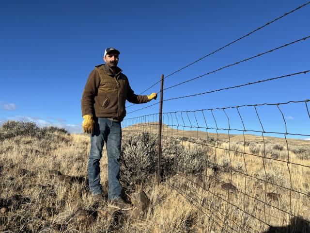 a man stands next to a barbed wire fence