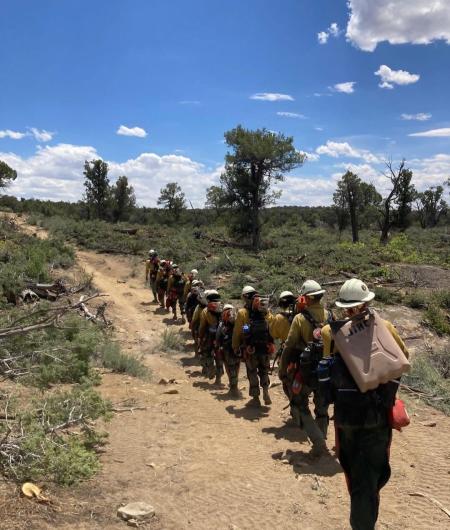 A group of BLM firefighters walk down a path carrying gear.