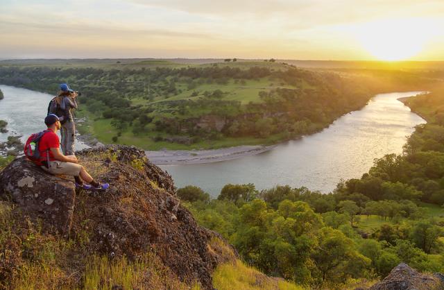 Sun sets over a river bed as two hikers look on