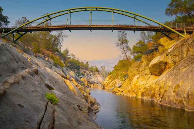 A bridge stretches over a deep, granite gorge at sunset.