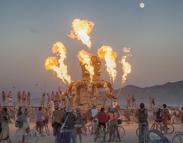 a burning art piece in a desert filled with people