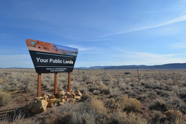 A sign saying "Your Public Lands - Bureau of Land Managment - Cedar City Field Office" on the landscape with blue sky above.