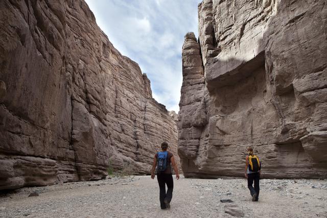 Two people walk through a wide and tall canyon